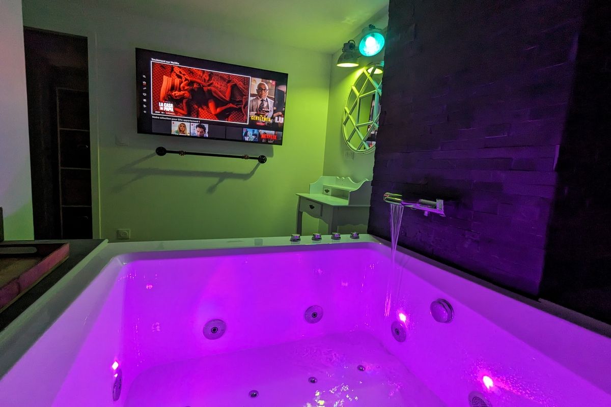 Ein Zimmer mit einer großen Badewanne, einem an der Wand befestigten Fernseher und einer grünen Wand.