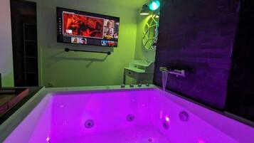 Ein Zimmer mit einer großen Badewanne, einem an der Wand befestigten Fernseher und einer grünen Wand.
