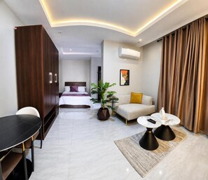 A modern hotel room with a bed, a sofa, a dining table, and a coffee table. - loftyzez luxury apartment  (Lekki)