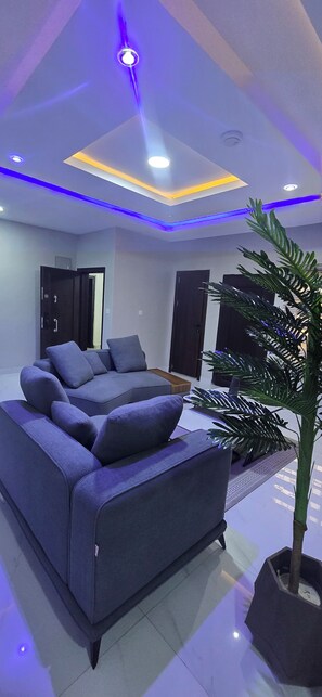 A modern bedroom with a sofa, a potted plant, and a ceiling with recessed lighting. - loftyzez luxury apartment  (Lekki)