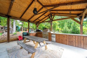 Un espace extérieur abrité comprenant une table de pique-nique, un barbecue et une vue sur une aire de jeux.