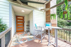 A covered porch with a wooden door, a white chair, a small table, and a metal railing. - Single Story Retreat with Pavilion (Chapel Hill)