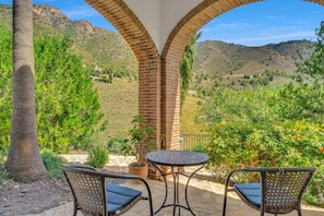 Eine Terrasse mit zwei Korbstühlen und einem Tisch, mit Blick auf eine gebirgige Landschaft.