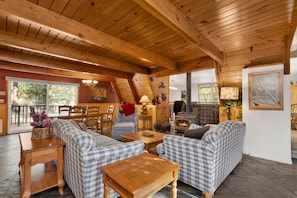 A cozy cabin interior with a wooden ceiling, a fireplace, checkered sofas, and a dining area. - Moose Moritz Manor #2667 (Big Bear Lake)