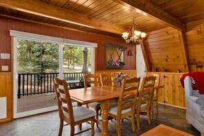 A wooden interior with a dining table and chairs, a chandelier, and a view through large windows. - Moose Moritz Manor #2667 (Big Bear Lake)