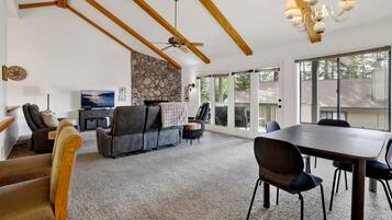 A modern living room with a stone fireplace, a ceiling fan, and a dining area with a table and chairs.
