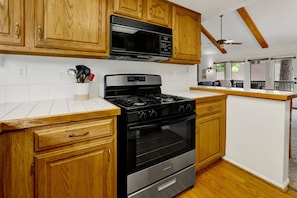 A kitchen with wooden cabinets, a stainless steel stove, and a microwave. - Powder & Putt Condo#2658 (Big Bear Lake)