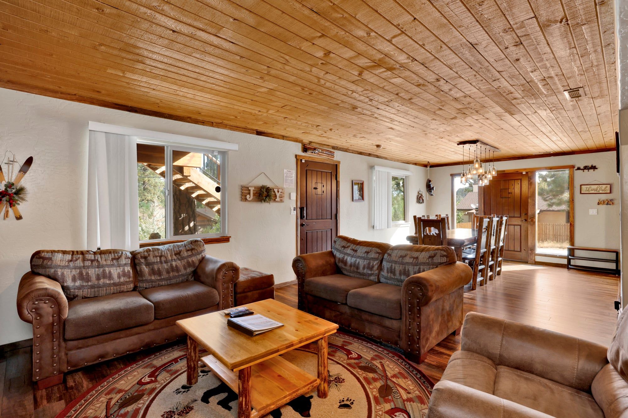 A spacious living room with a high wooden ceiling, leather sofas, a wooden coffee table, and a dining area with wooden chairs.