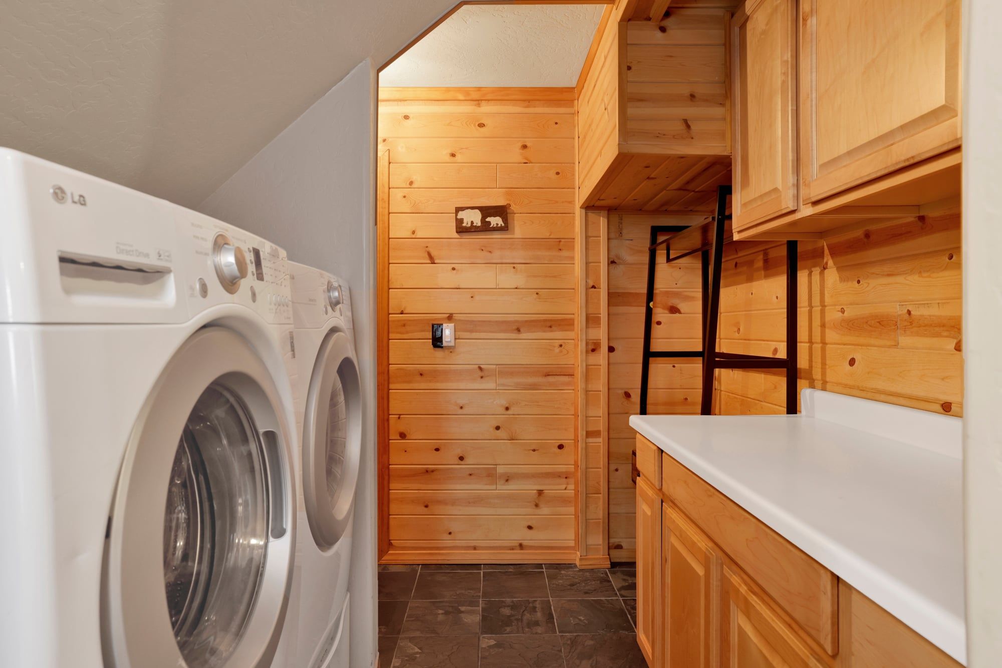 A compact laundry area with a front-loading washing machine, wooden cabinets, and a small shelf.