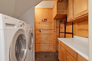 Un espace buanderie compact comprenant un lave-linge à chargement frontal, des armoires en bois et une petite étagère.