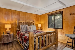 Ein Zimmer mit Holzboden, einem Bett, zwei Nachttischlampen, einem Fenster und einem Sessel.