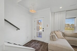 A modern living room with a staircase, a chandelier, a sofa with cushions, and a window with curtains. - Stay Sunny | Bikes, 1-2 min Beachwalk, NEW (Panama City Beach)