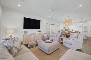 A modern living room with a flat-screen TV, comfortable seating, a dining area, and a kitchen with white cabinets. - Stay Sunny | Bikes, 1-2 min Beachwalk, NEW (Panama City Beach)