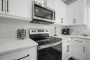 A modern kitchen with white cabinetry, a stainless steel microwave, a built-in oven, and a coffee maker. - Stay Sunny | Bikes, 1-2 min Beachwalk, NEW (Panama City Beach)