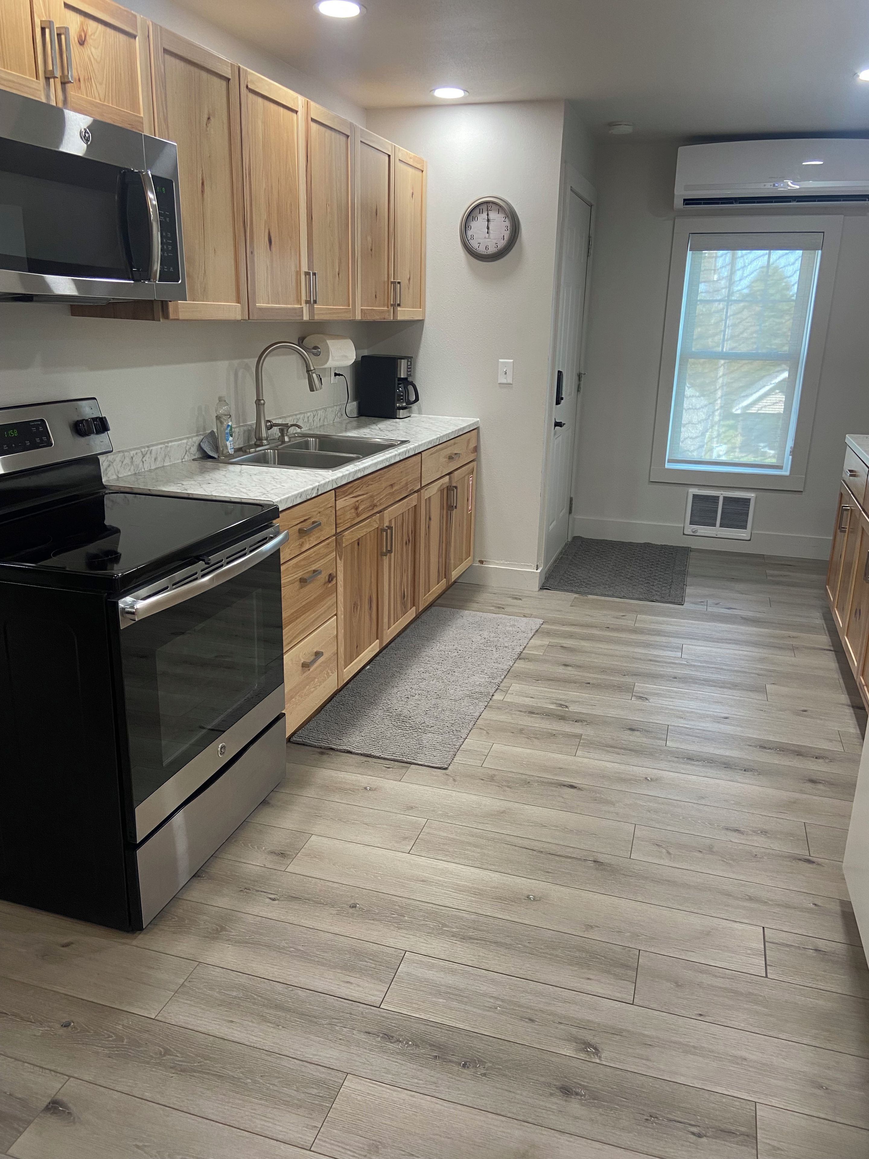 A kitchen with wooden cabinets, stainless steel appliances, a clock, and a window.
