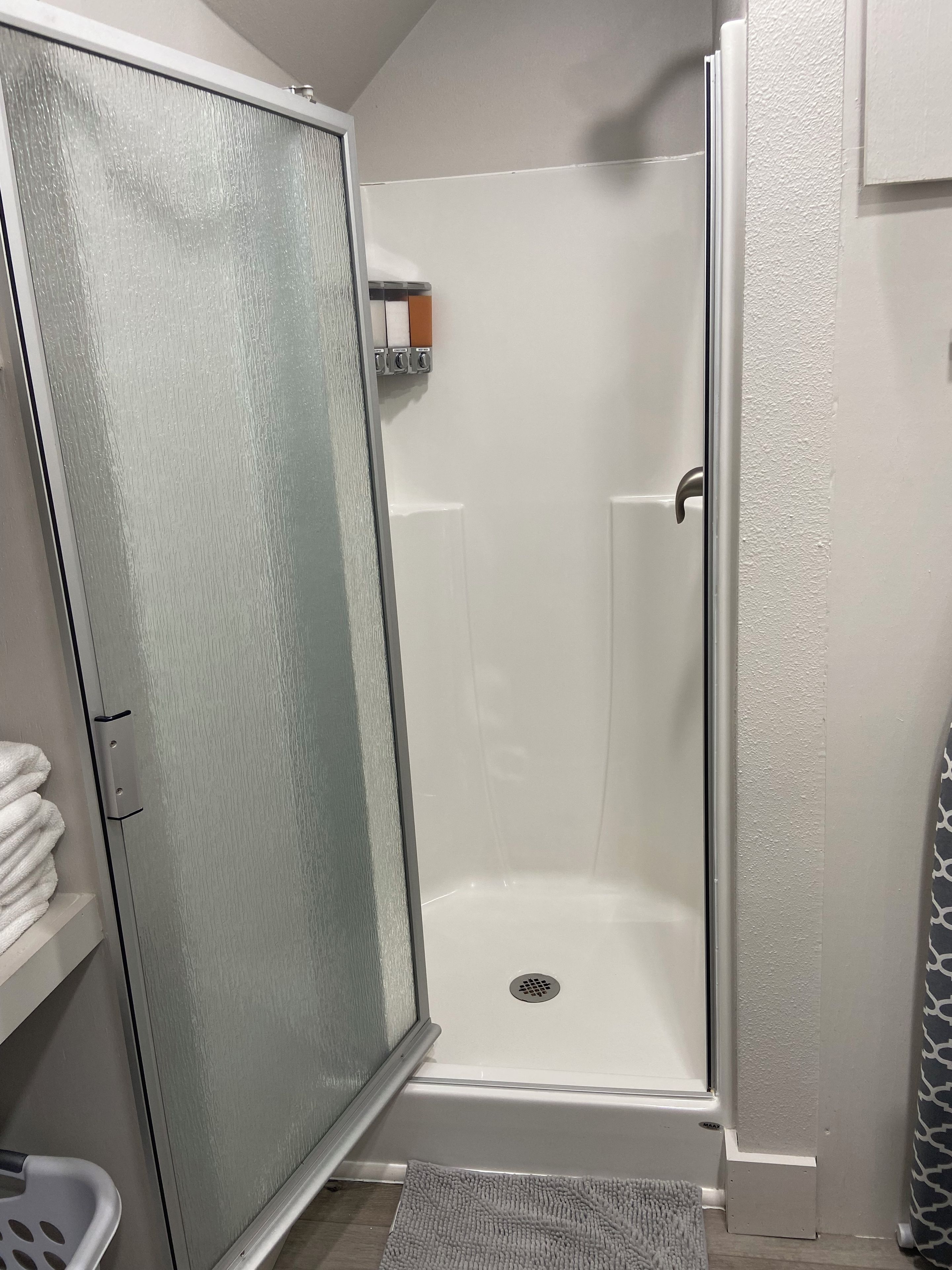A bathroom with a glass shower enclosure, a white towel rack, and a patterned shower curtain.