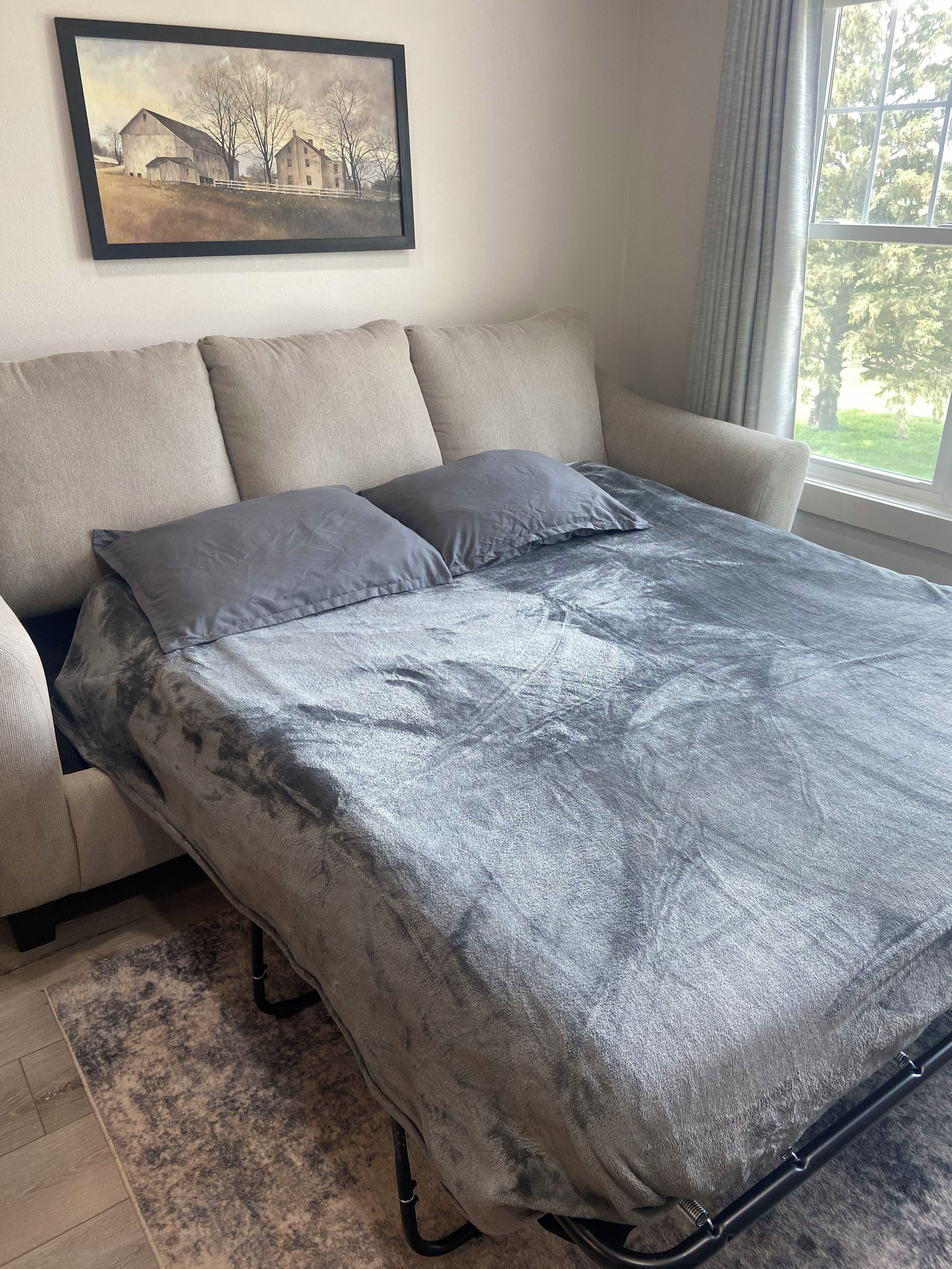 Un lit avec une couvre-lit grise, une tête de lit et une fenêtre avec des rideaux.