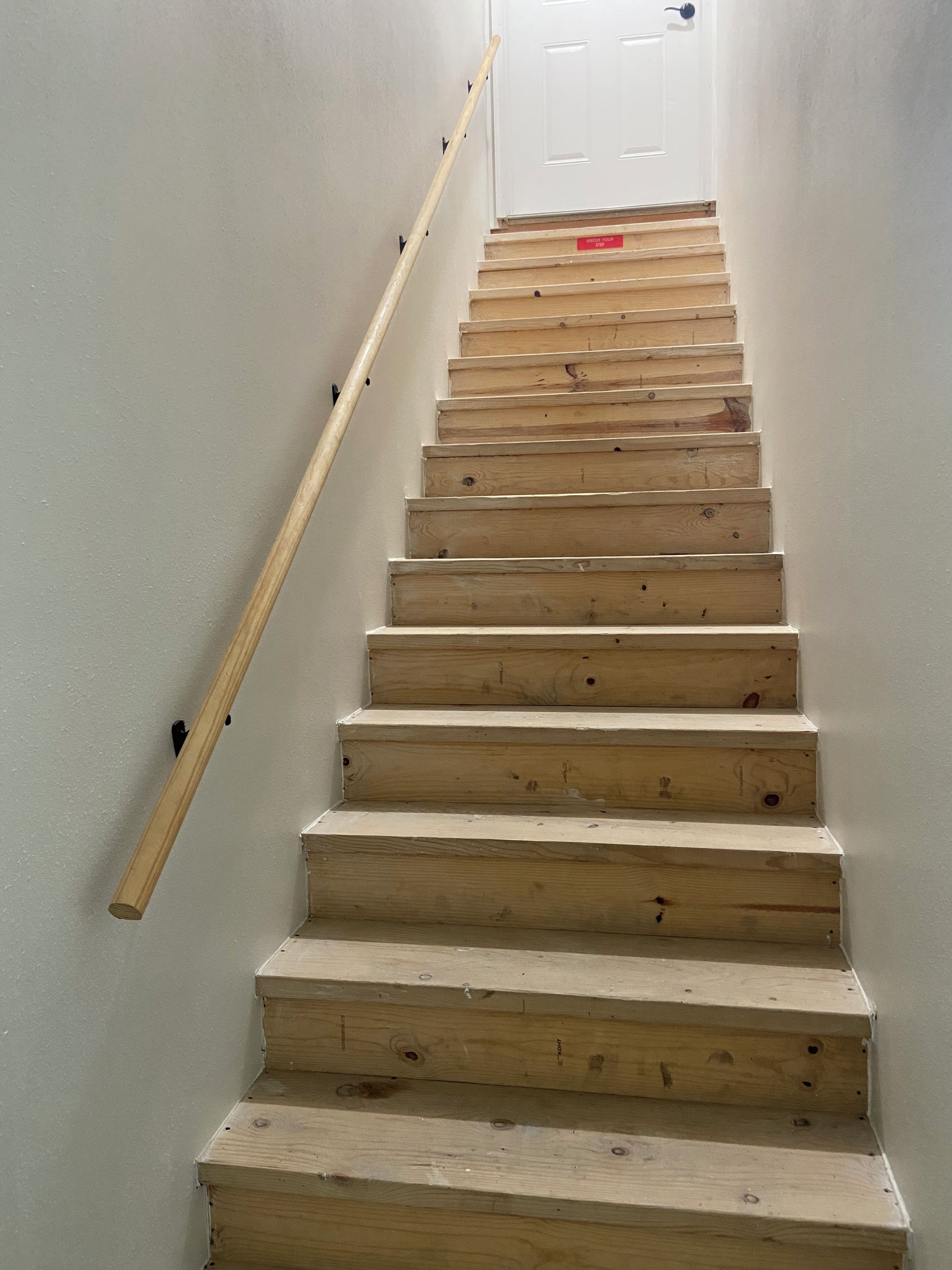 Una escala de fusta amb barana que condueix a una porta blanca al final.