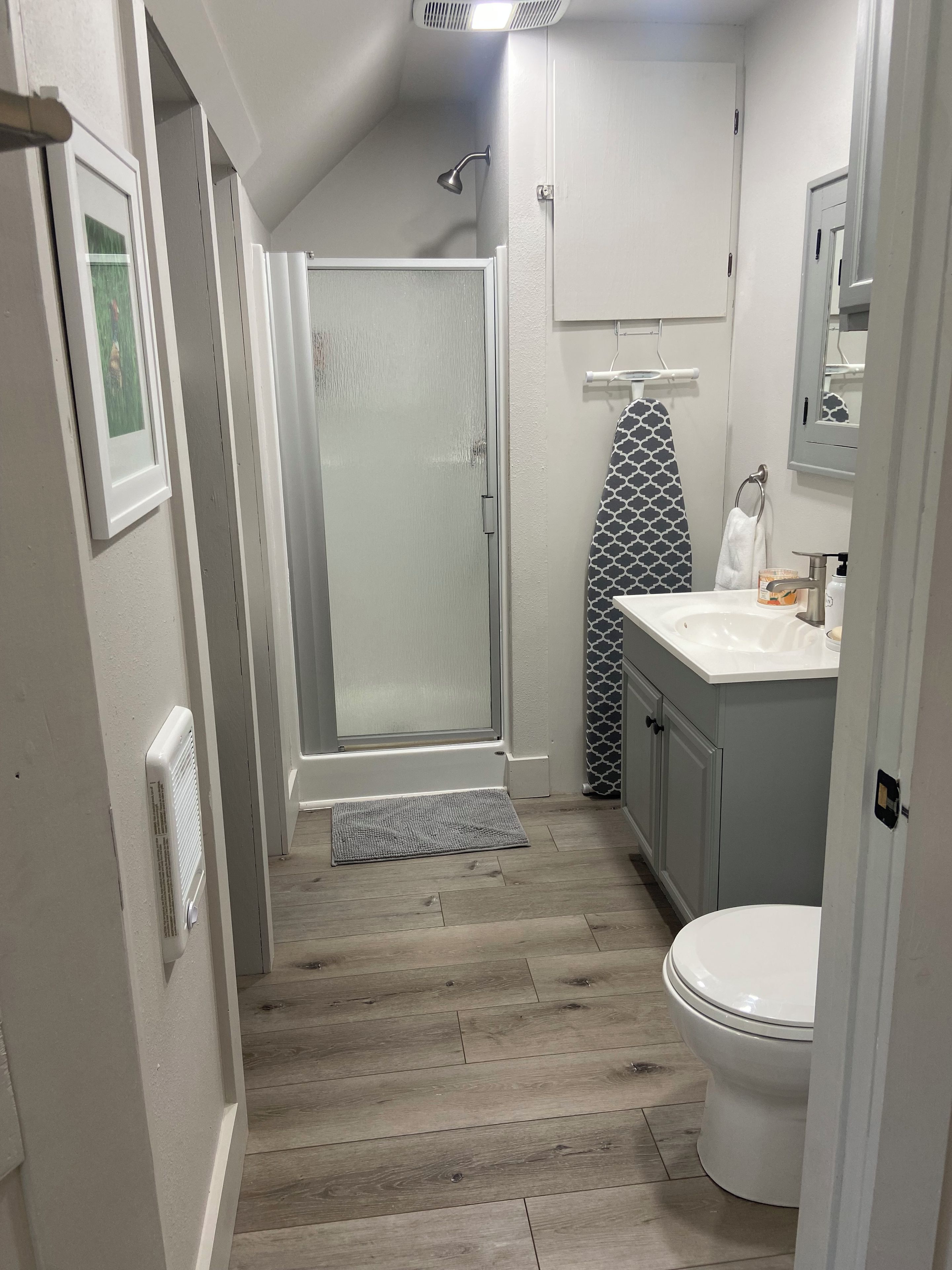 A narrow hallway leading to a bathroom with a shower, toilet, and vanity.