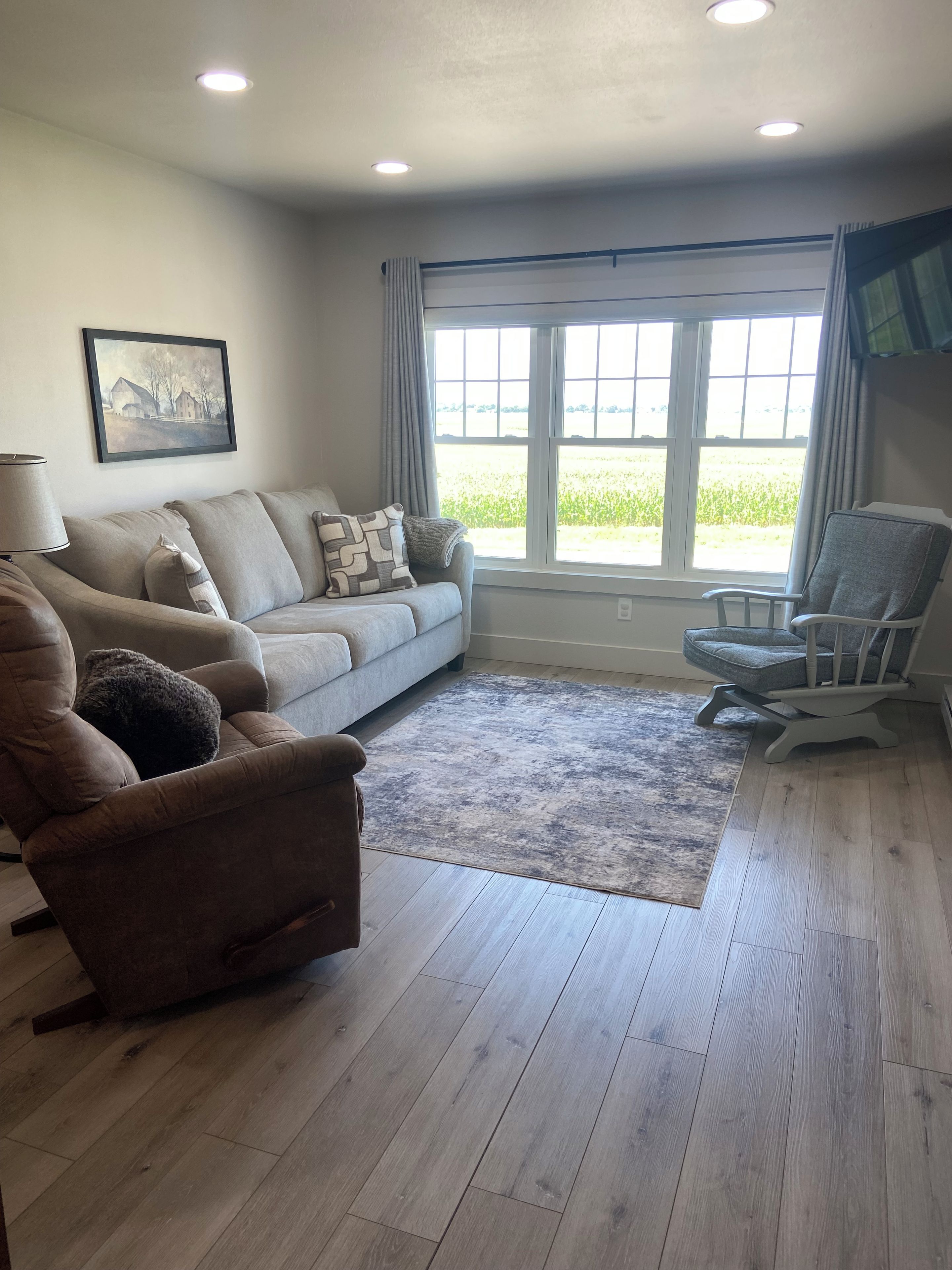 A living room with a sofa, armchair, and a large window with curtains.