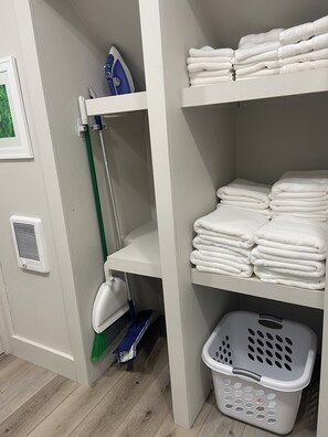 A laundry area with a shelf of folded towels, a mop, and a laundry basket. - Cozy studio loft apartment in rural Iowa with beautiful sunrise and sunset views (Clearfield)