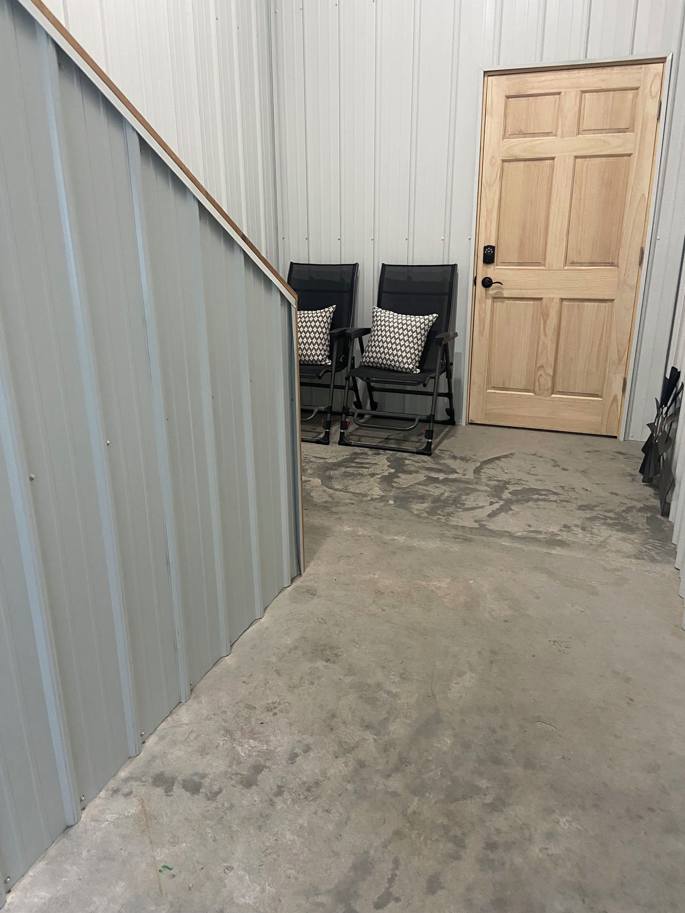 A corridor with a metal wall, a wooden door, and two black chairs with patterned cushions.