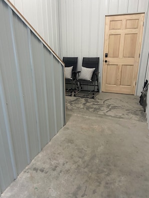 A corridor with a metal wall, a wooden door, and two black chairs with patterned cushions.