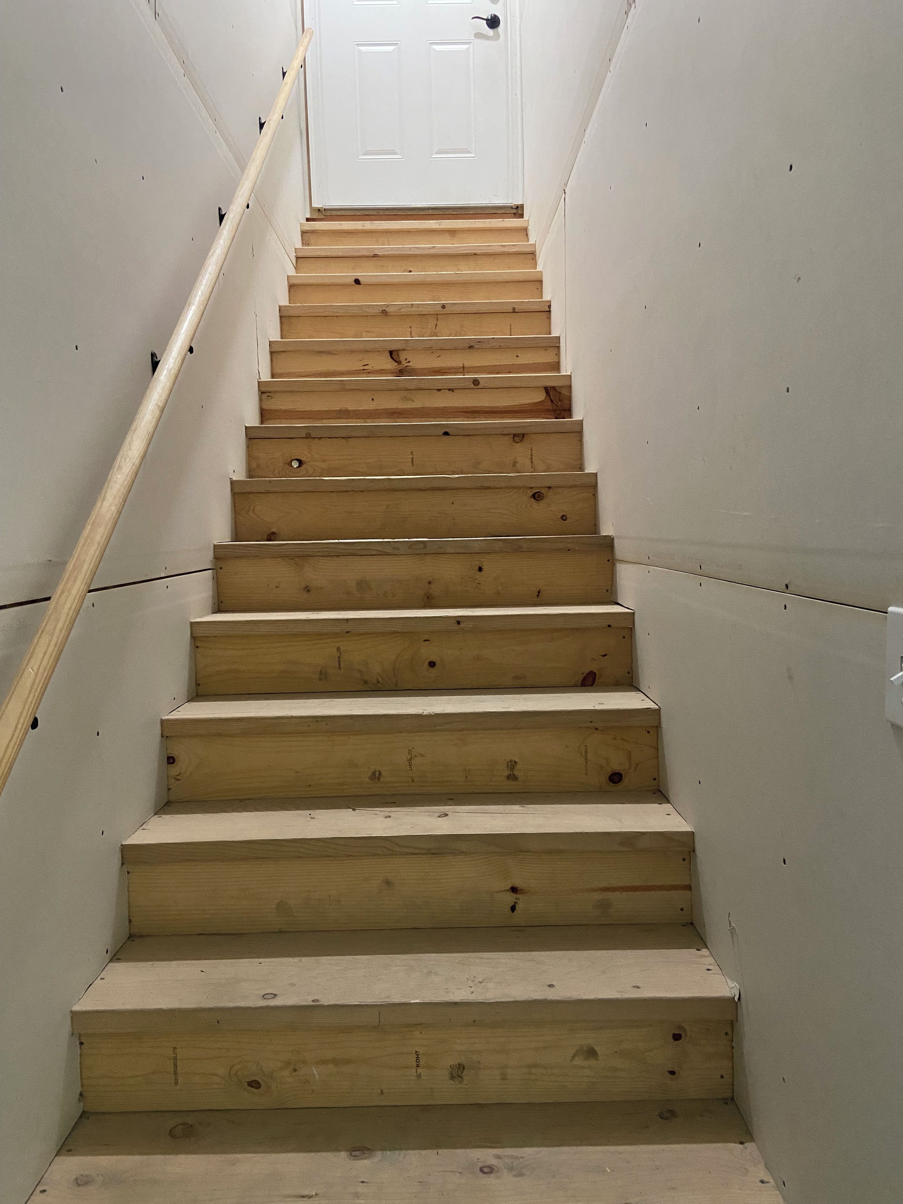 Un escalier en bois mène à une porte blanche.