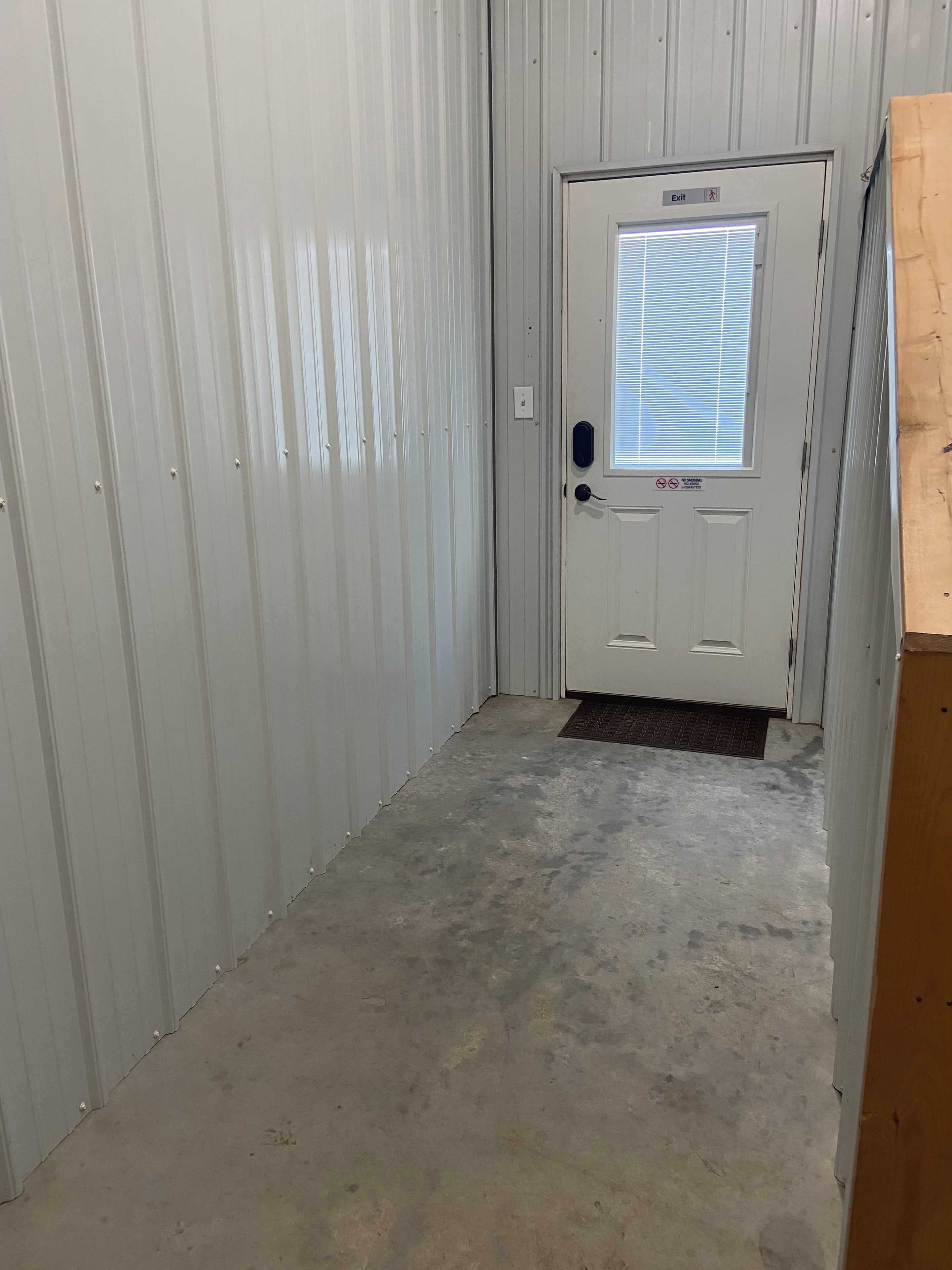 A hallway with a white door, a window with blinds, and a doormat.