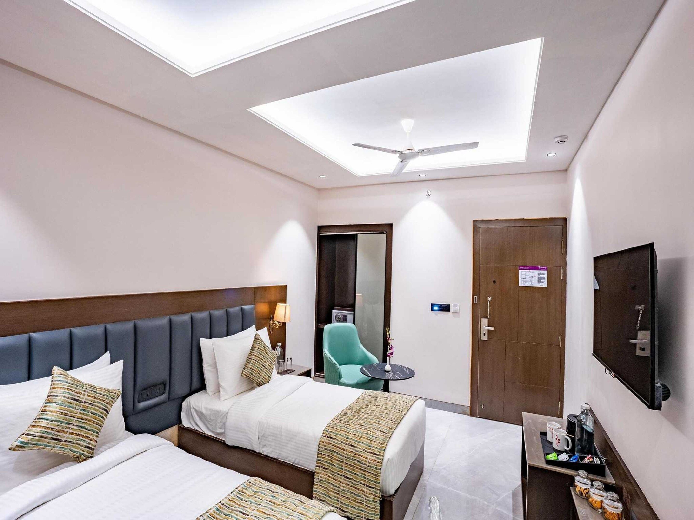 A hotel room with two beds, a ceiling fan, a TV, and a small table with a coffee maker.