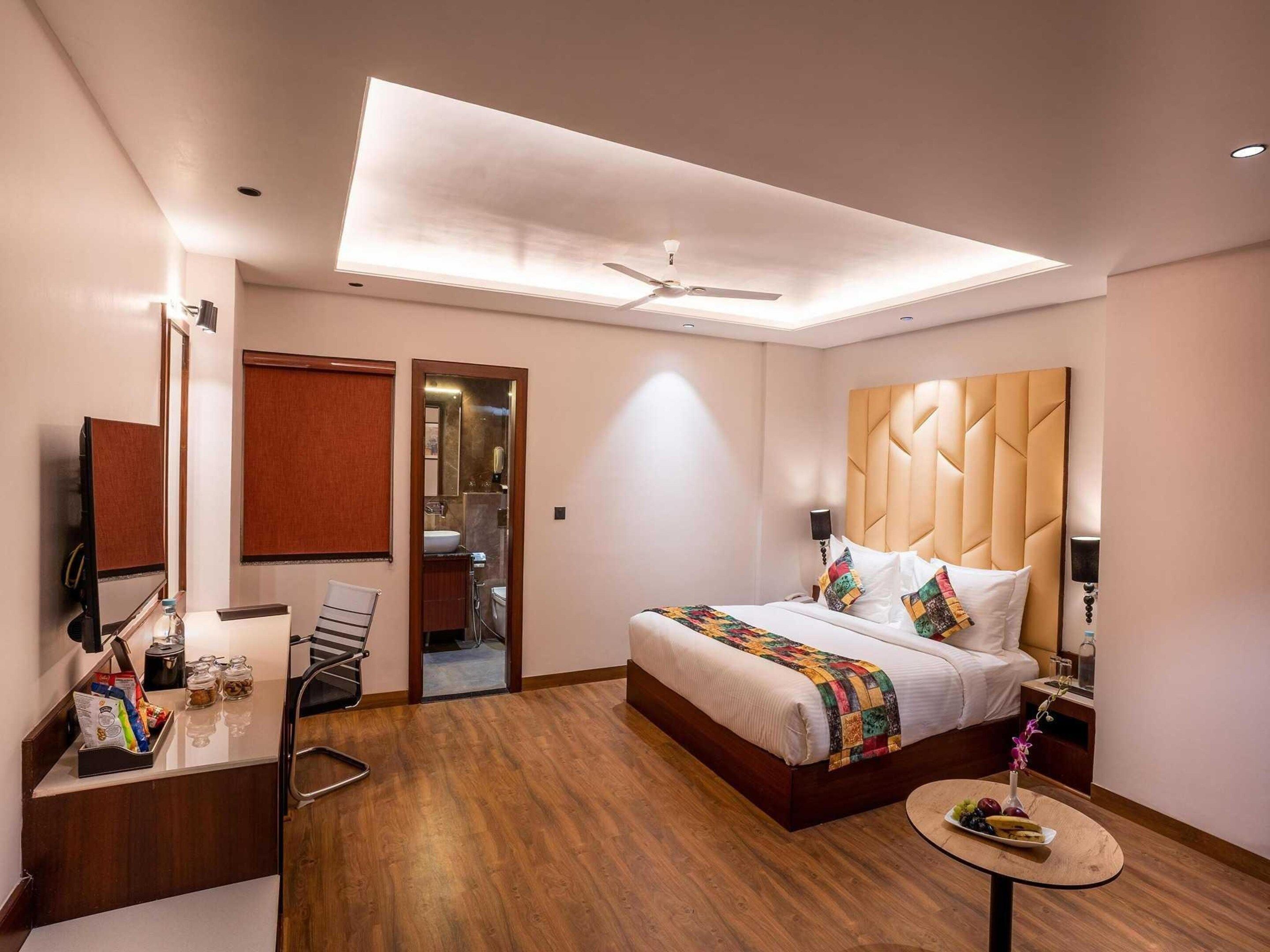 A hotel room with a bed, bedside table, mirror, and a small round table with fruit.