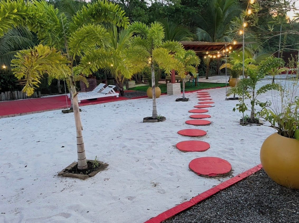 Un sendero flanqueado por escalones circulares rojos que conducen a una zona de estar con sillones blancos.