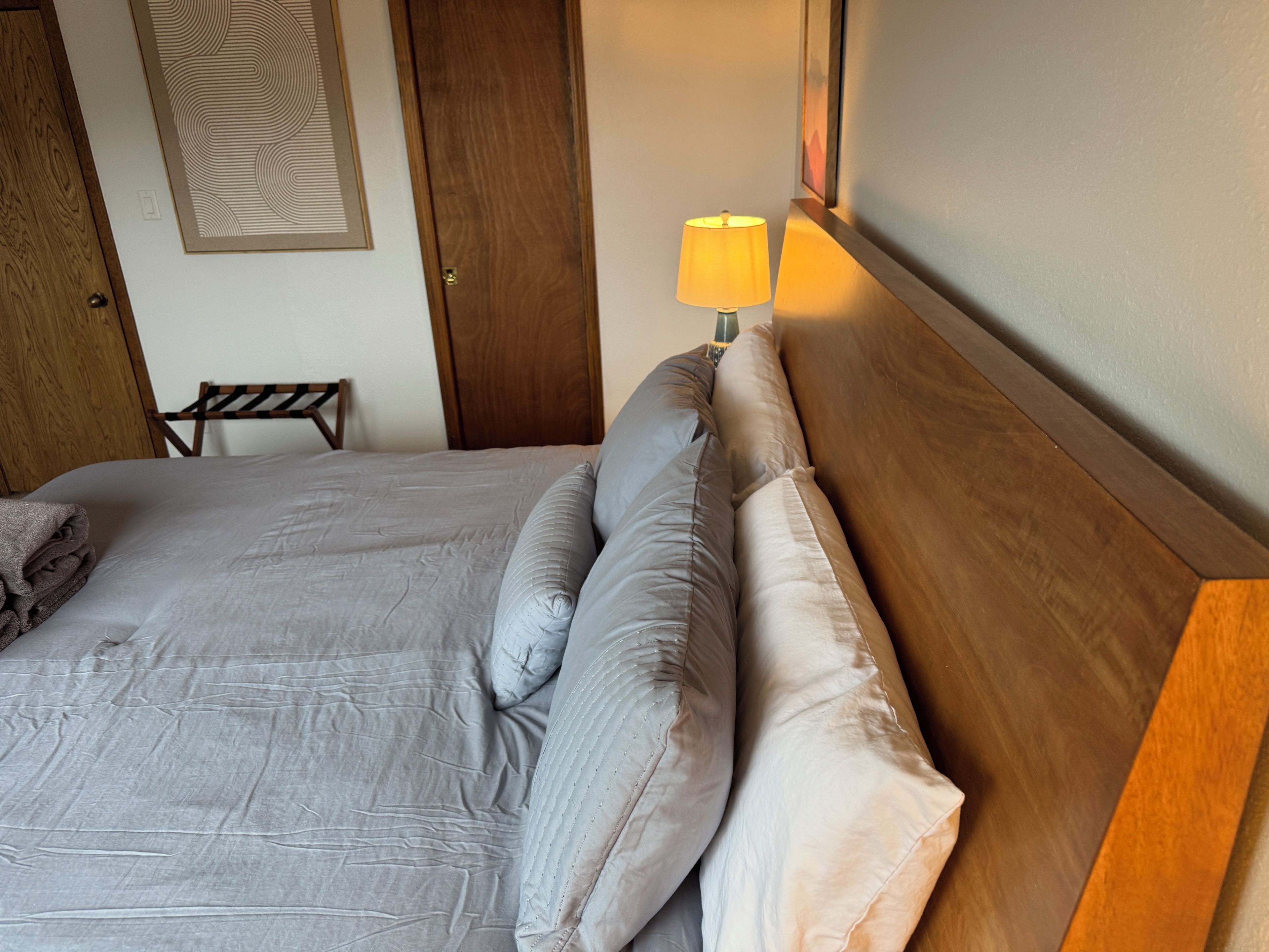 Un lit bien fait, avec une tête de lit, une lampe de chevet et une serviette pliée posée sur le côté gauche.