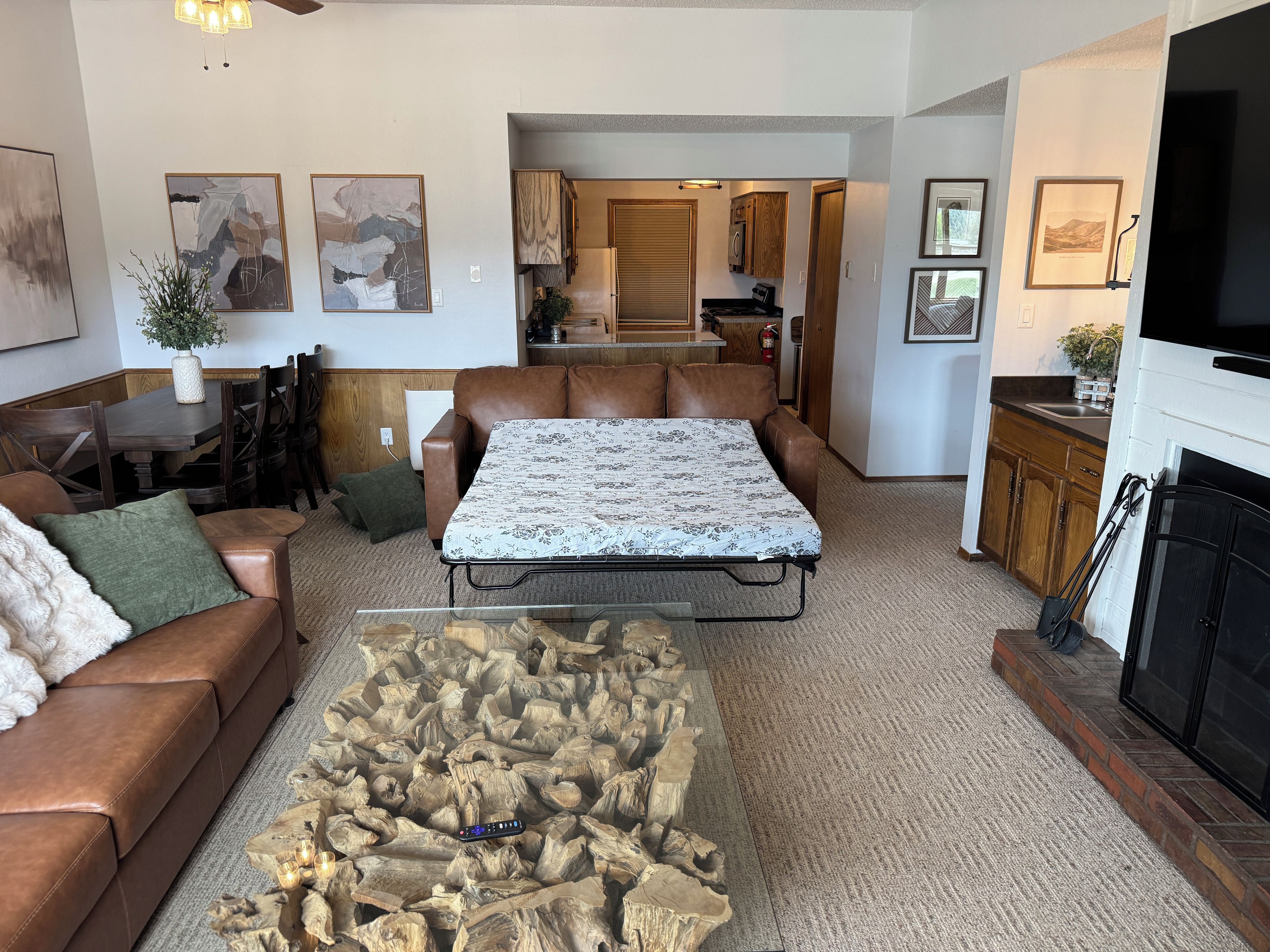 Een woonkamer met een bruine leren bank, een salontafel met een houten decoratie, en een eethoek met een tafel en stoelen.