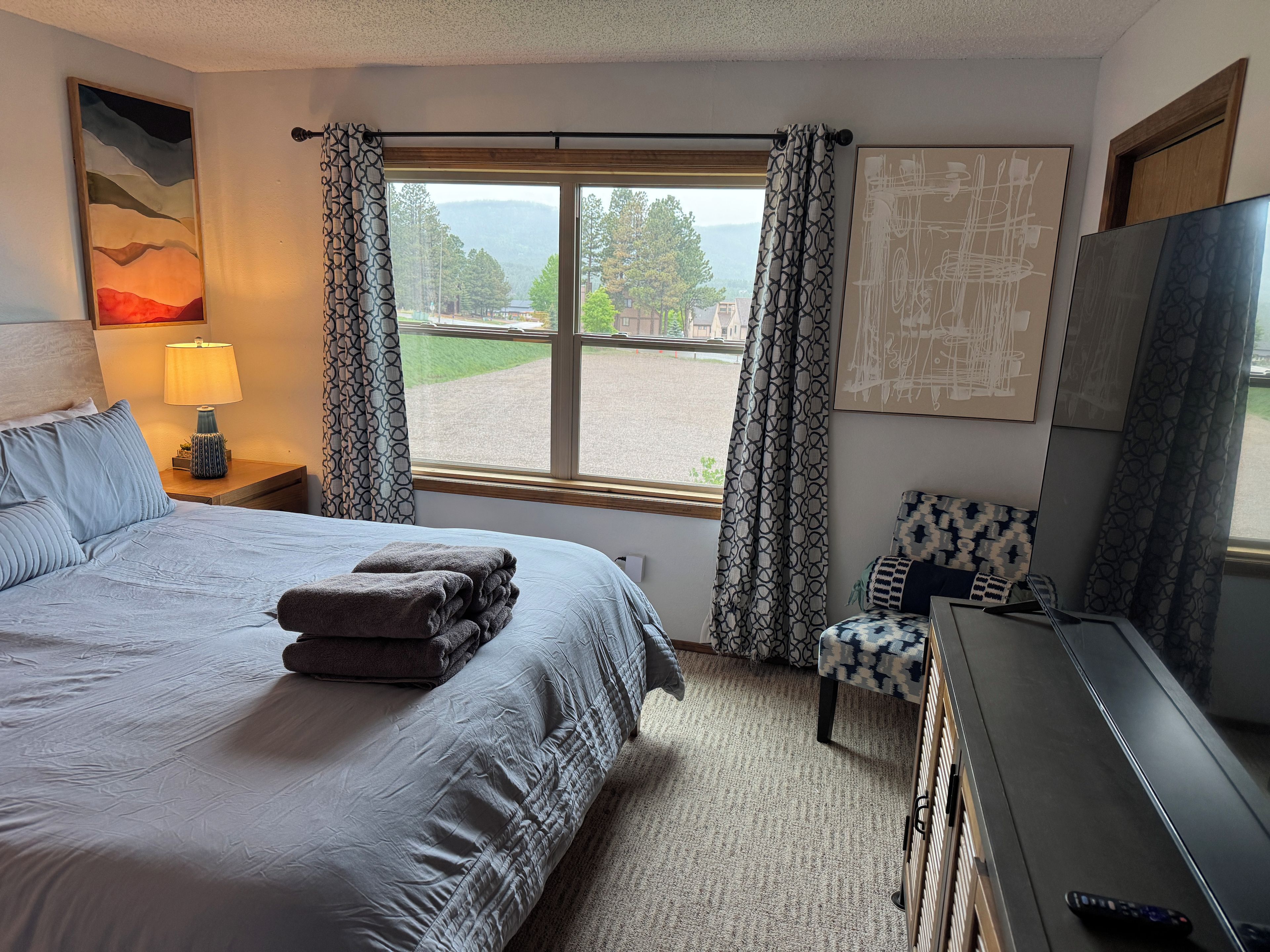 A hotel room with a bed, a desk, a chair, a TV, and a window with curtains.