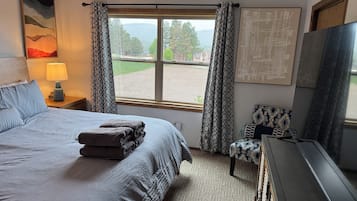 A hotel room with a bed, a desk, a chair, a TV, and a window with curtains.