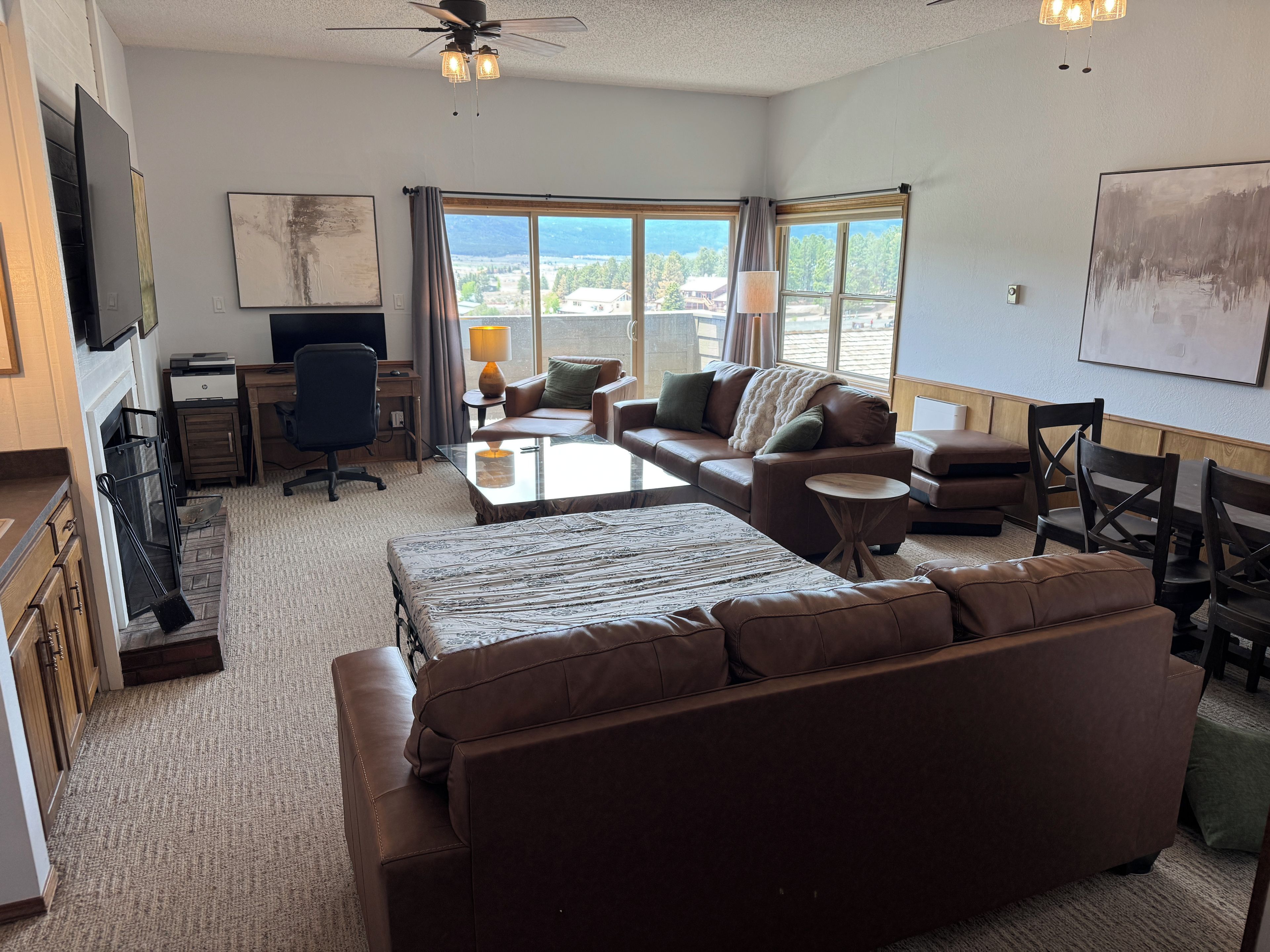 A modern living room with a large window, a sofa, a coffee table, and a desk with a chair.