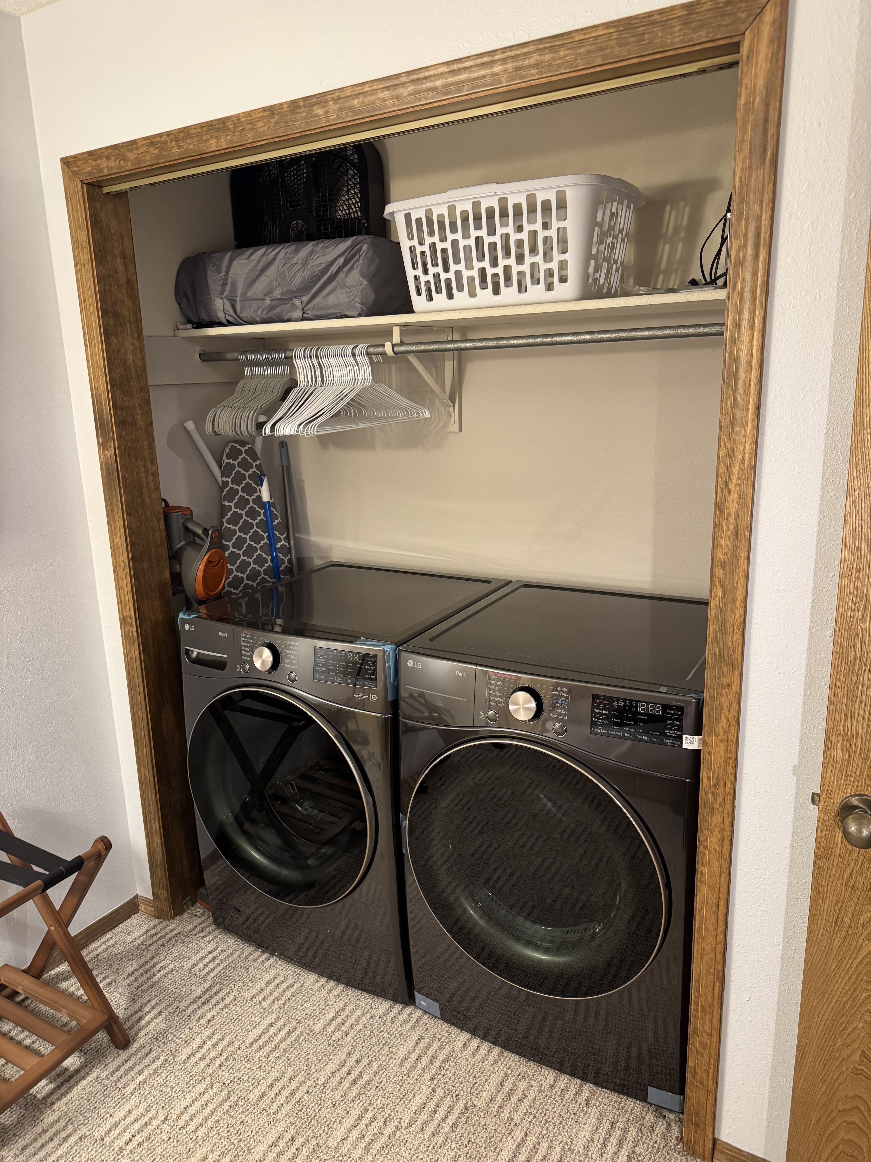 A laundry area with two front-loading washing machines, a drying rack, and a shelf with laundry baskets.