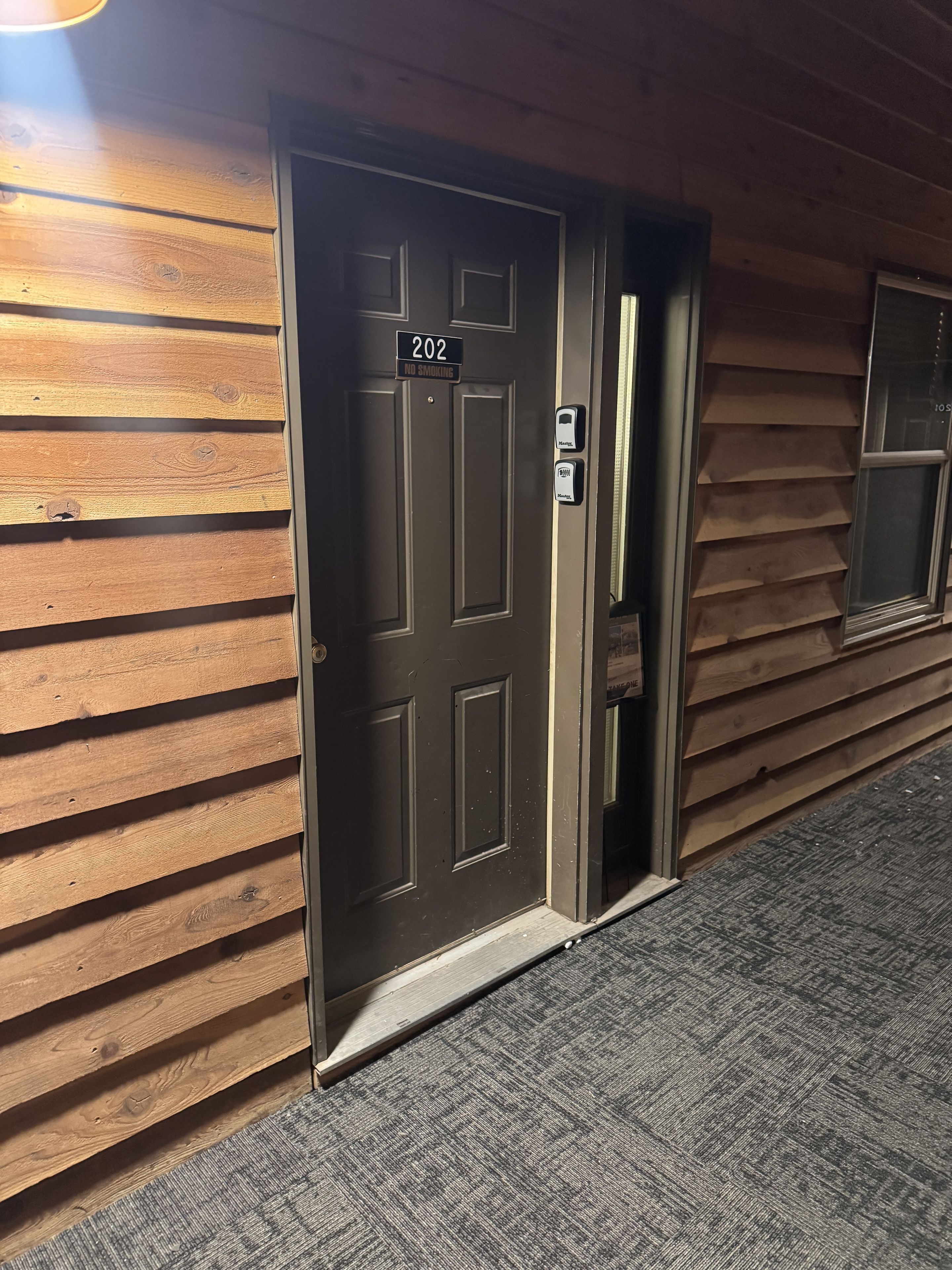 A wooden exterior wall with a door labeled '202 NO SMOKING' and a doorbell.