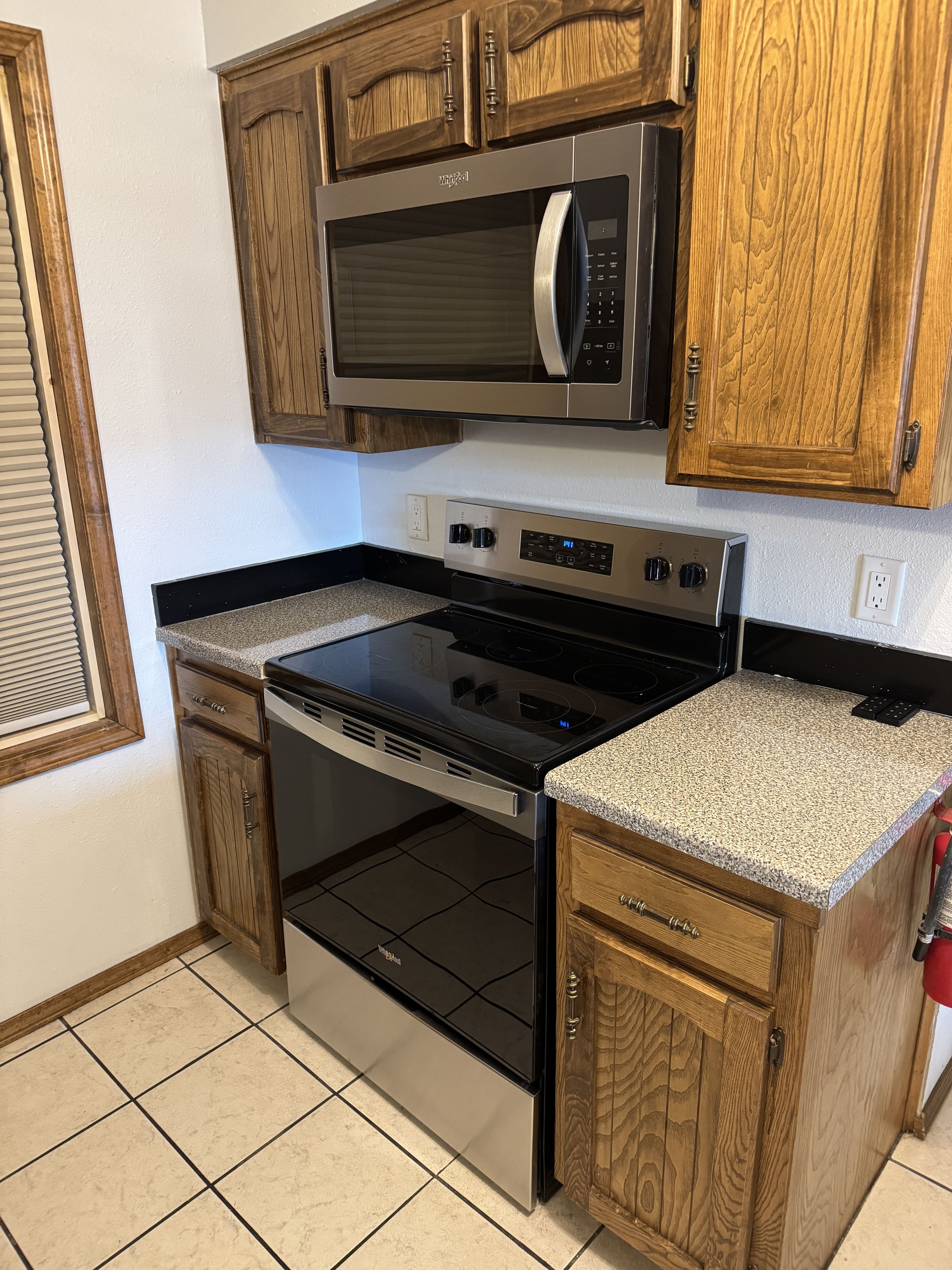 A kitchen with wooden cabinets, a stainless steel microwave, a stove, and a granite countertop.