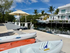 A marina with kayaks docked, a covered area with an umbrella, and a building with a balcony overlooking the water. - Gulfside Canal-front Fishing destination with Private Dockage (Marathon)
