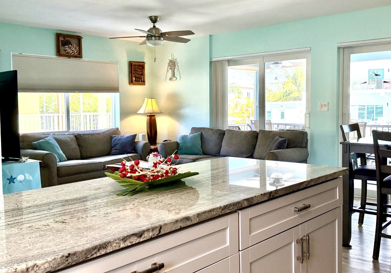 A modern kitchen with a marble countertop, a dining area with a table and chairs, and a living room with a sofa and a TV.