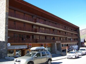 Ein mehrgeschossiges Hotel mit Balkonen, einem Café und mehreren parkenden Autos davor.