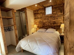 Ein Schlafzimmer mit Holz-Kopfteil, einem Bett mit weißer Bettwäsche, einem Nachttisch mit Lampe und einem Fenster mit Vorhängen.