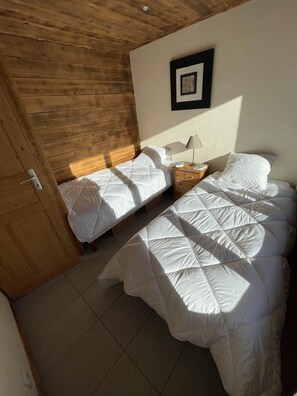 Ein Schlafzimmer mit zwei Betten, einer Holzbalkendecke, einem gerahmten Bild an der Wand und einem Nachttisch mit Lampe.