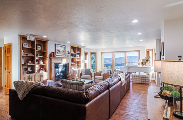 A spacious living room with a fireplace, a piano, and a view of the mountains.