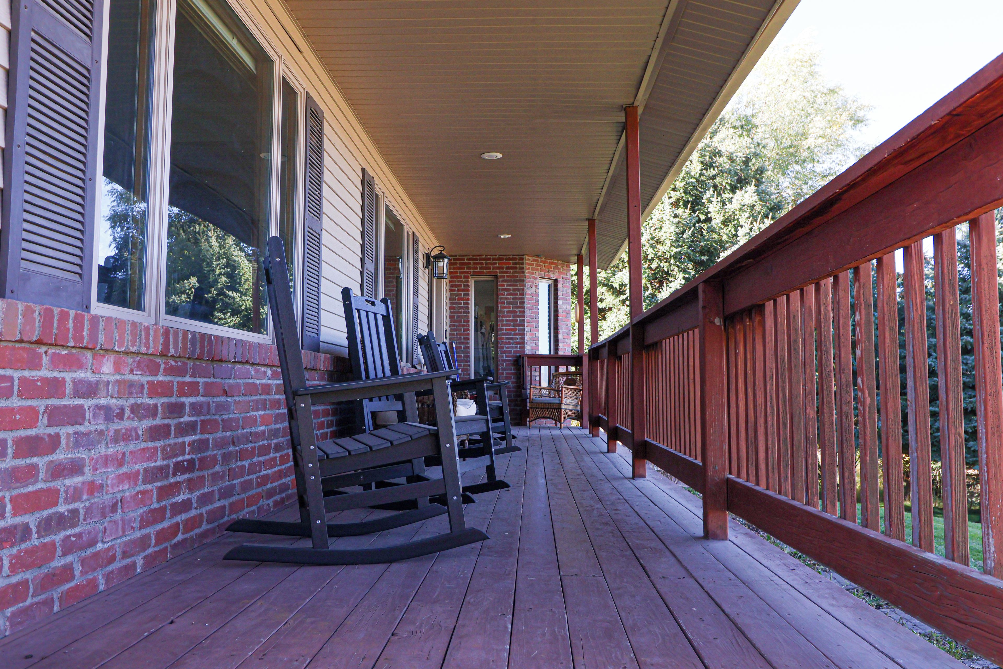 A covered porch with wooden railings, a brick wall, and a wooden deck.