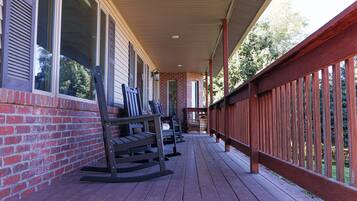 A covered porch with wooden railings, a brick wall, and a wooden deck.