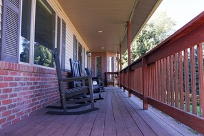 A covered porch with wooden railings, a brick wall, and a wooden deck.