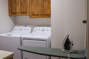 A laundry area with two white washing machines and an iron on a green ironing board. - Willowsprings Ranch Lodge, Sleeps 24 + Pool (Ririe)